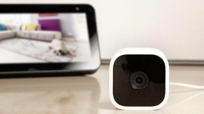 Blink Mini smart kamera på et bord med en Fire tablet i baggrunden